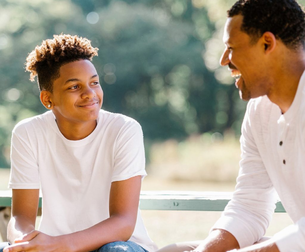 Adult and teenager sitting outdoors and smiling while having a supportive conversation.